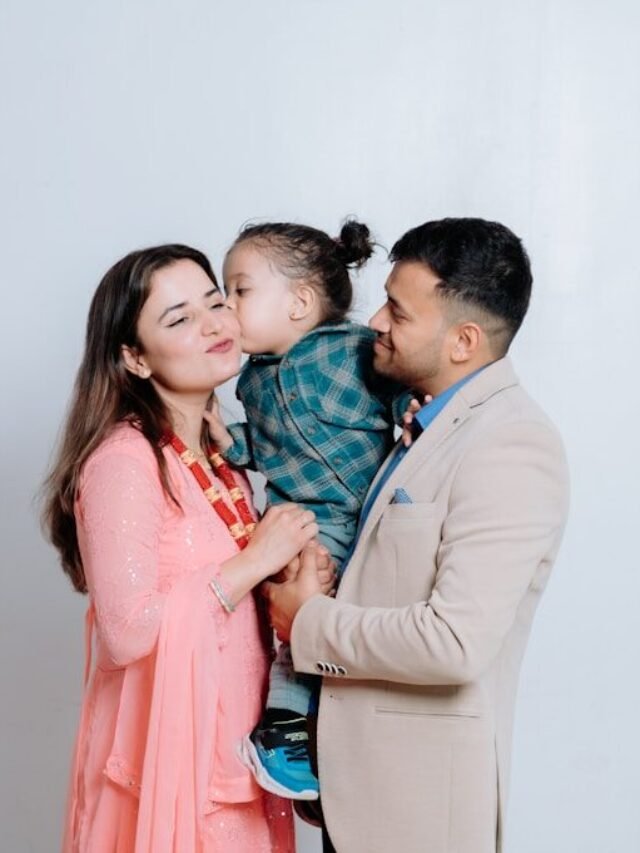 A man and a woman holding a baby in front of a white wall